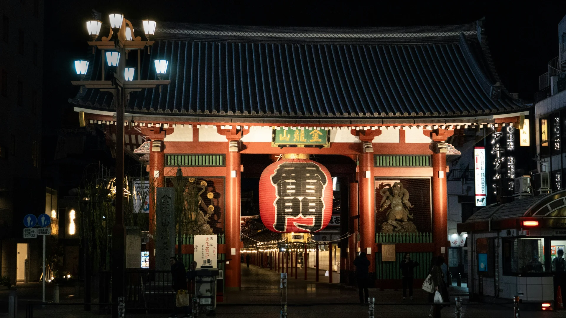 The Kaminarimon gate in Asakusa at night, its giant red lantern glowing between two statues beneath a dark tiled roof